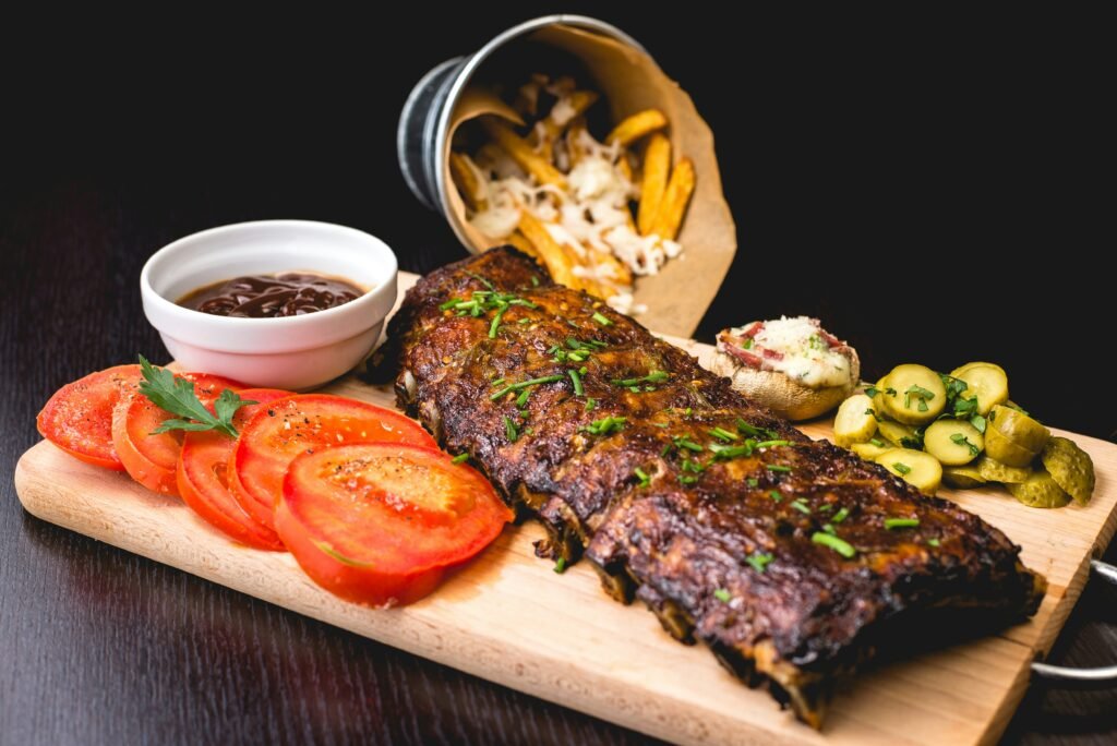 Rack of glazed ribs served on a wooden board with tomatoes, pickles, fries and sauce