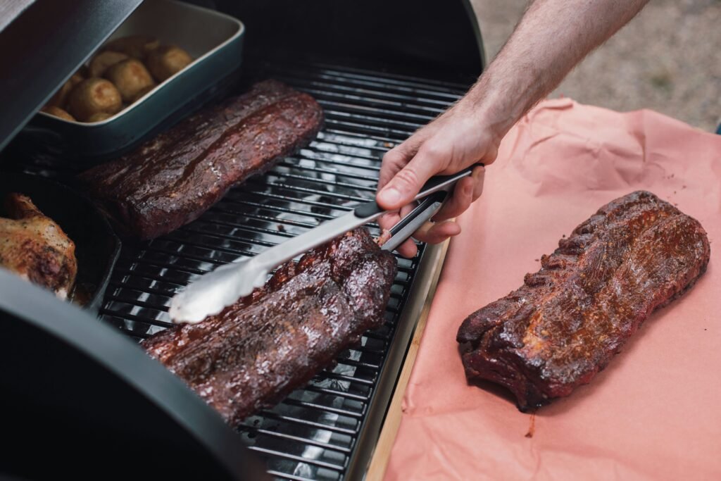 Smoked ribs being lifted off the smoker onto butcher paper