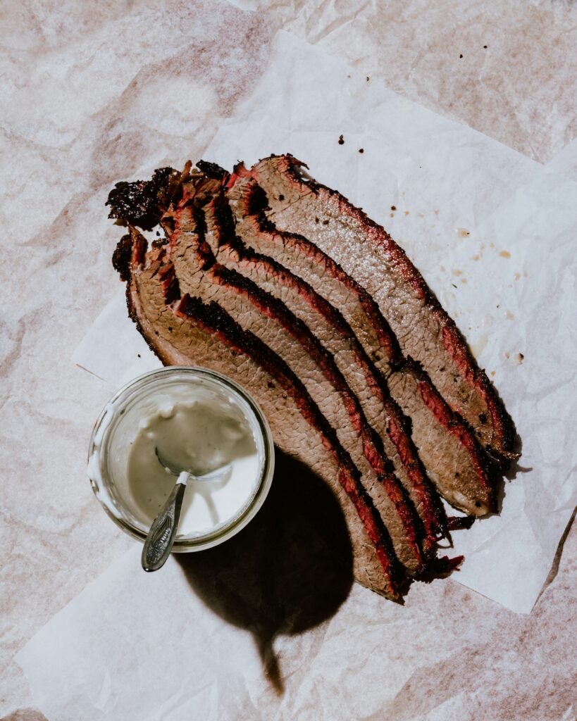 Slices of smoked brisket on butcher paper with a cup of sauce